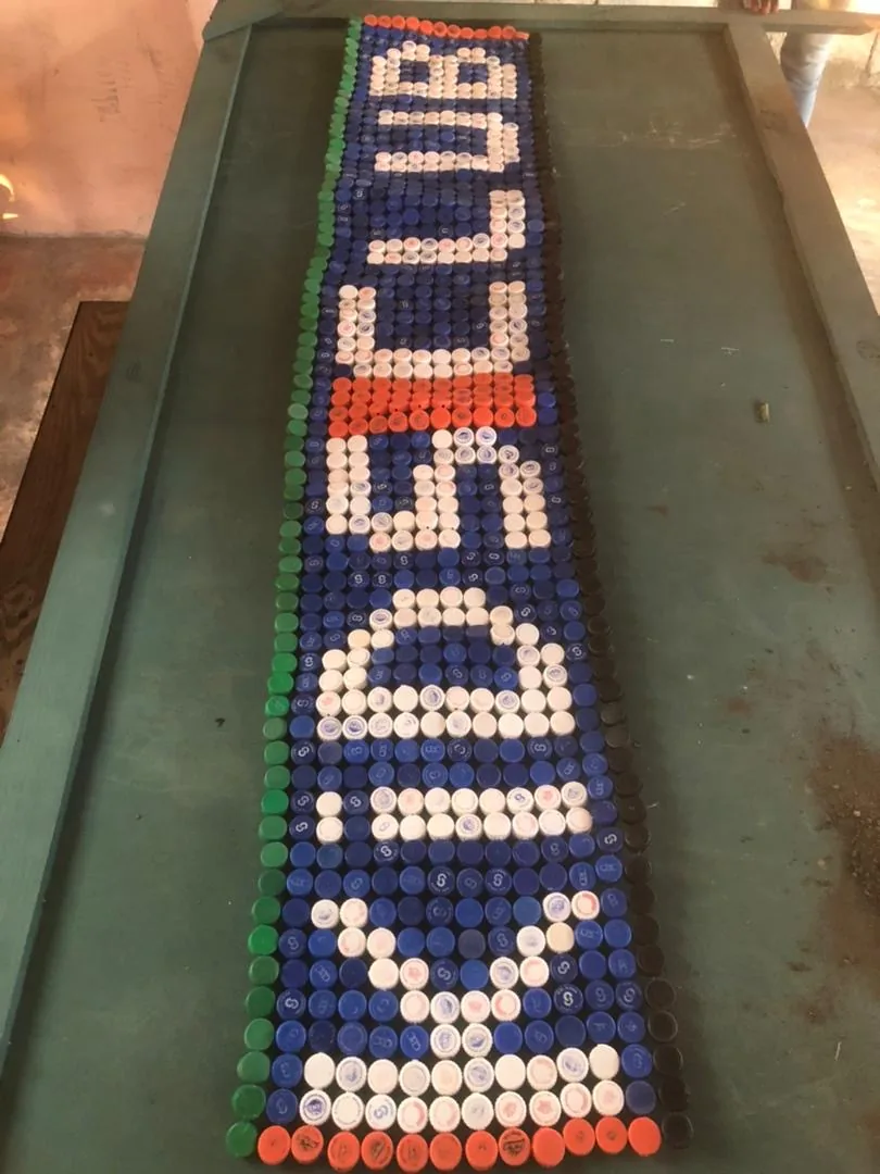 Recycled bottle-cap mural spelling Kids Club Haiti